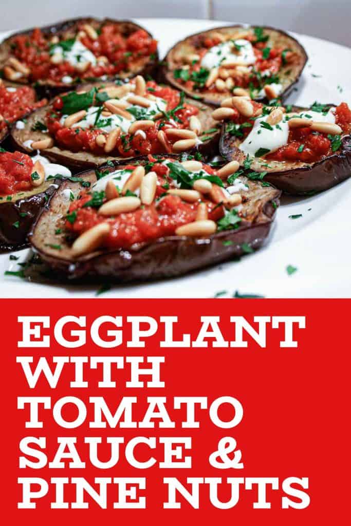 A platter of sliced and roasted eggplant topped with tomato sauce, yoghurt and roasted pine nuts with a final garnish of chopped parsley.