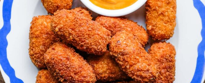A blue rimmed platter of Spanish jamon croquetas with a smoked paprika alioli on the side.