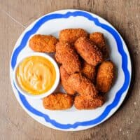 A blue rimmed platter of Spanish jamon croquetas with a smoked paprika alioli on the side.