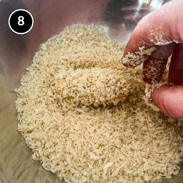 A croqueta being dredged in breadcrumbs