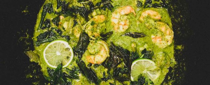A pan of green masala with shrimp scattered with fried curry leaves and lime slices