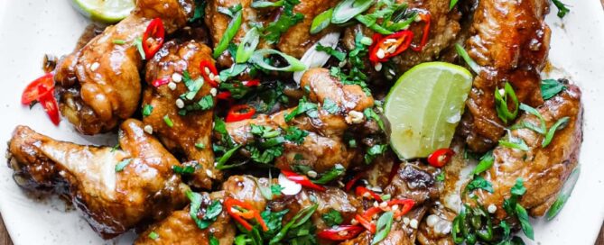 A platter of Indonesian chicken wings garnished with cilantro, chillies and spring onion alongside some lime wedges.