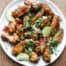 A platter of Indonesian chicken wings garnished with cilantro, chillies and spring onion alongside some lime wedges.