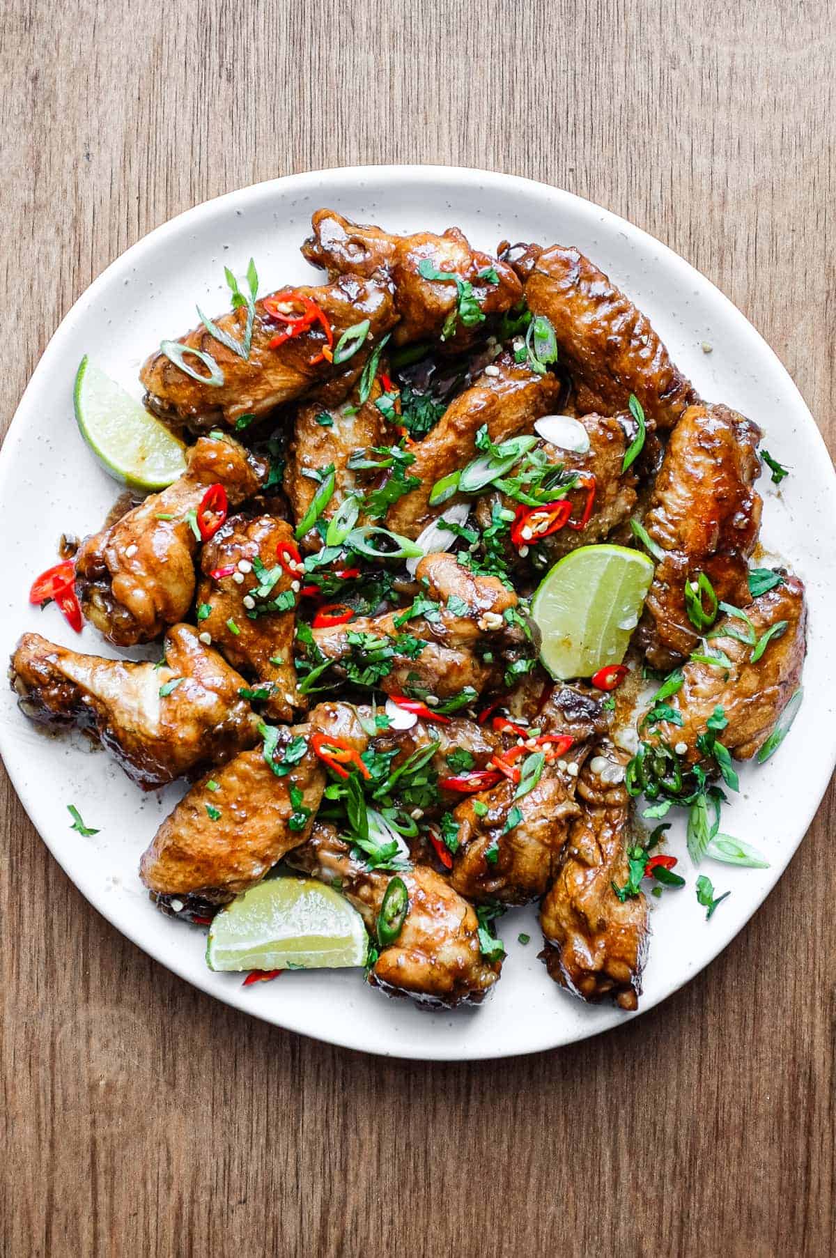 A platter of Indonesian chicken wings garnished with cilantro, chillies and spring onion alongside some lime wedges.