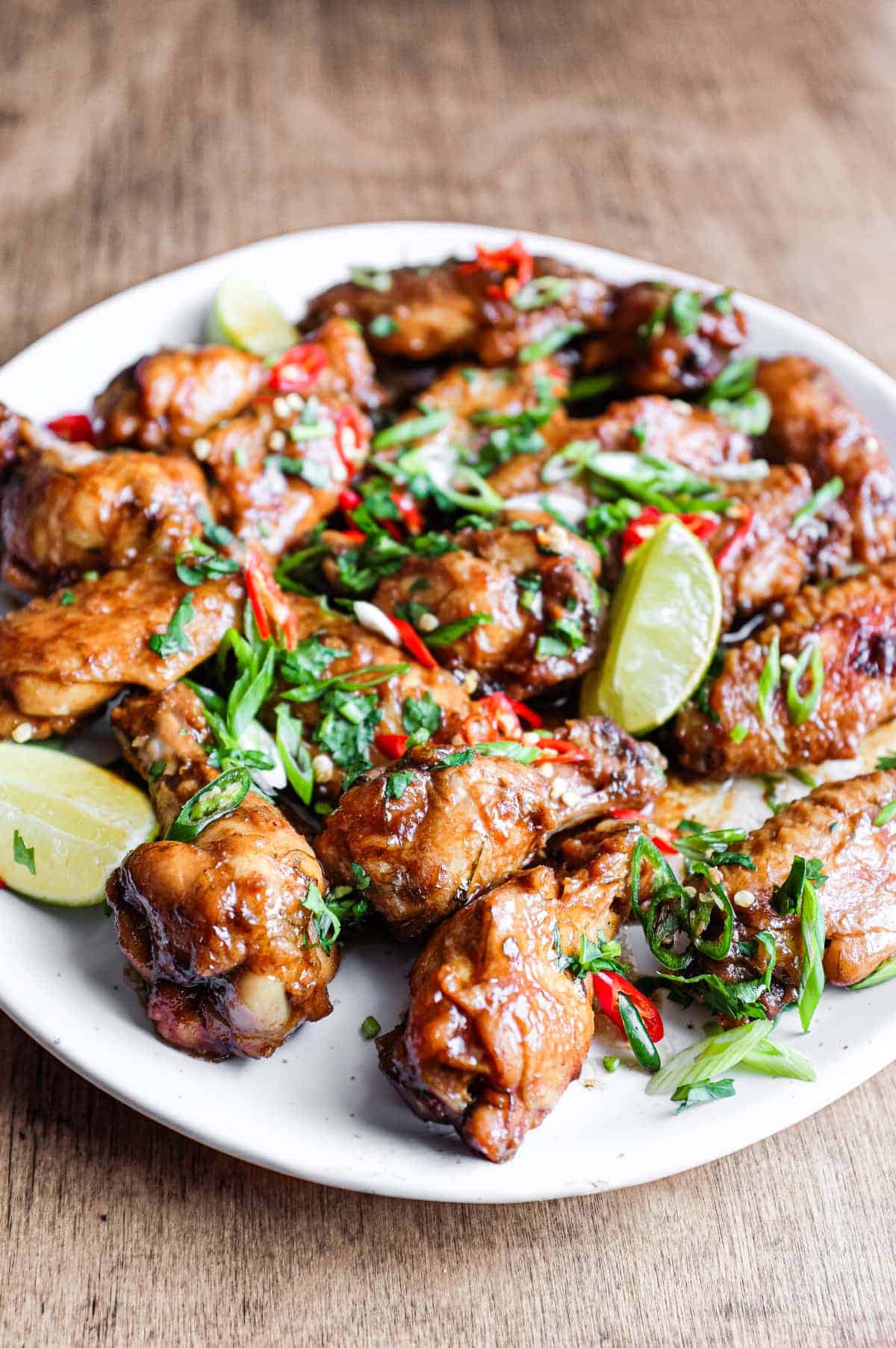 A platter of Indonesian chicken wings garnished with cilantro, chillies and spring onion alongside some lime wedges.