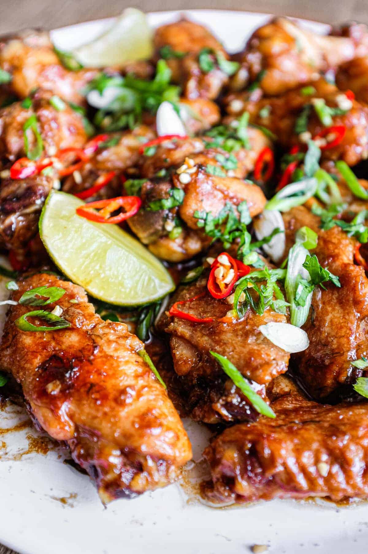 A platter of Indonesian chicken wings garnished with cilantro, chillies and spring onion alongside some lime wedges.