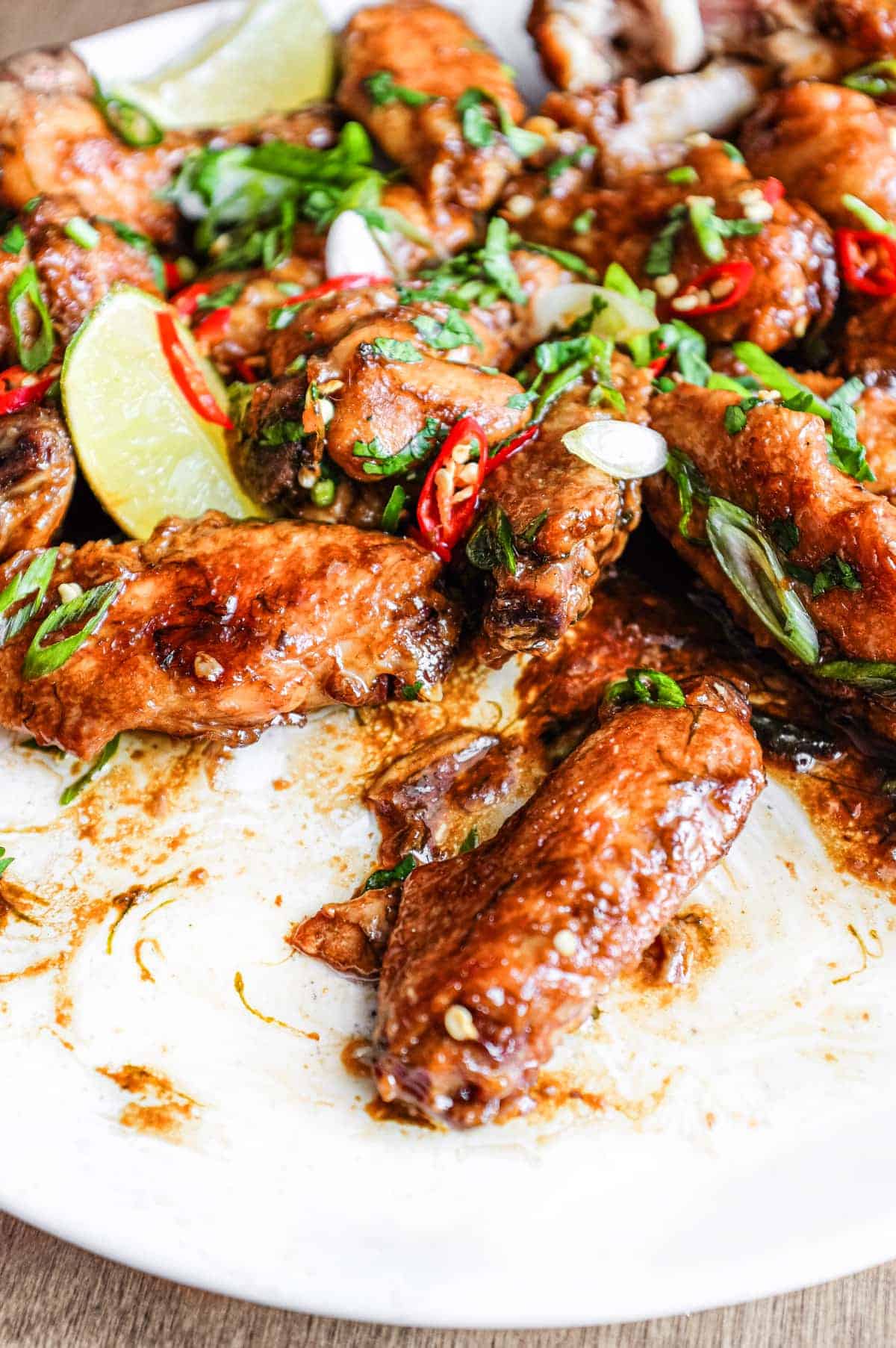 A platter of Indonesian chicken wings garnished with cilantro, chillies and spring onion alongside some lime wedges.