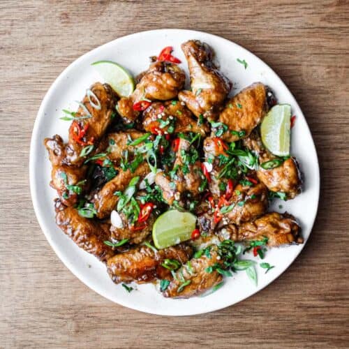 A platter of Indonesian chicken wings garnished with cilantro, chillies and spring onion alongside some lime wedges.