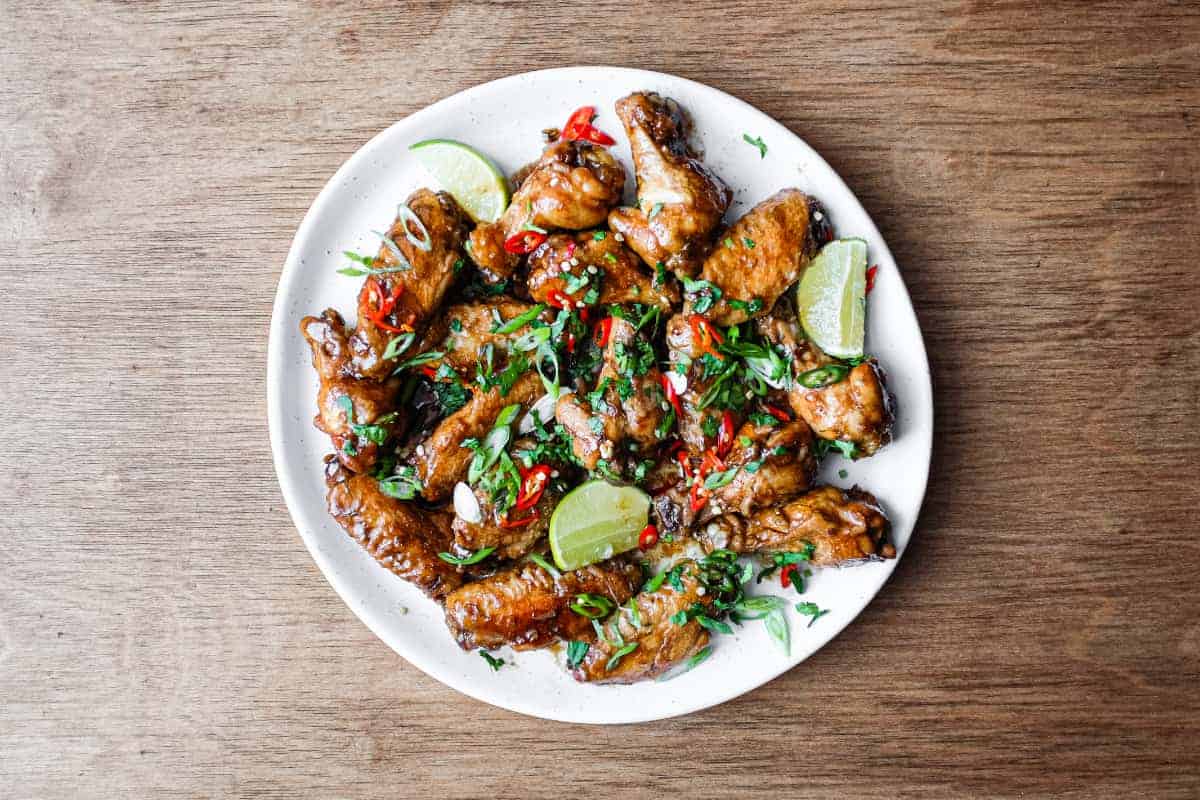 A platter of Indonesian chicken wings garnished with cilantro, chillies and spring onion alongside some lime wedges.