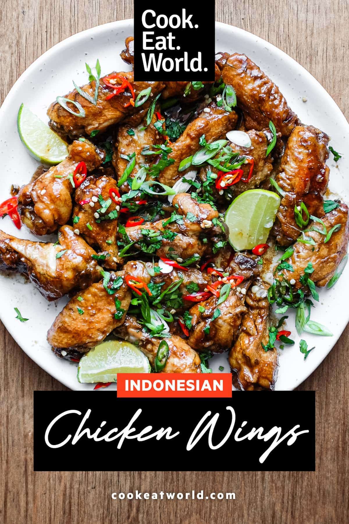 A platter of Indonesian chicken wings garnished with cilantro, chillies and spring onion alongside some lime wedges.