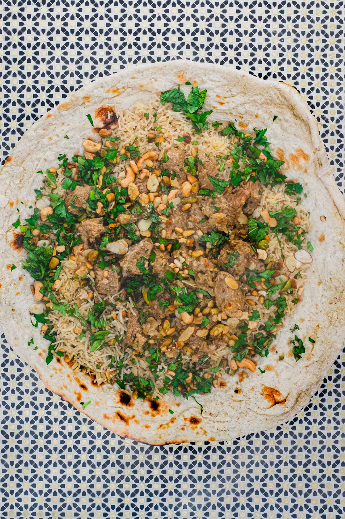 Jordanian lamb Mansaf stew sits on a giant flatbread. It's garnished with fresh herbs and toasted nuts.