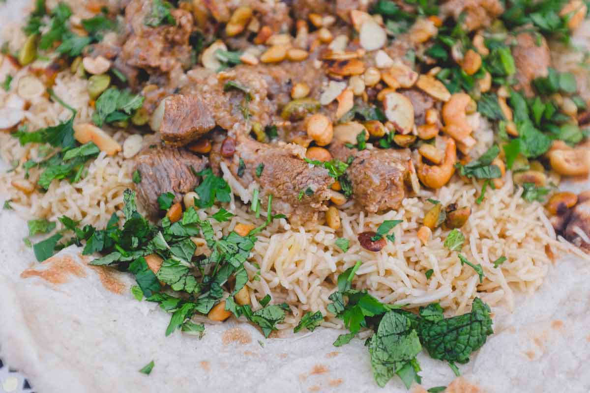 Jordanian lamb Mansaf stew sits on a giant flatbread. It's garnished with fresh herbs and toasted nuts.