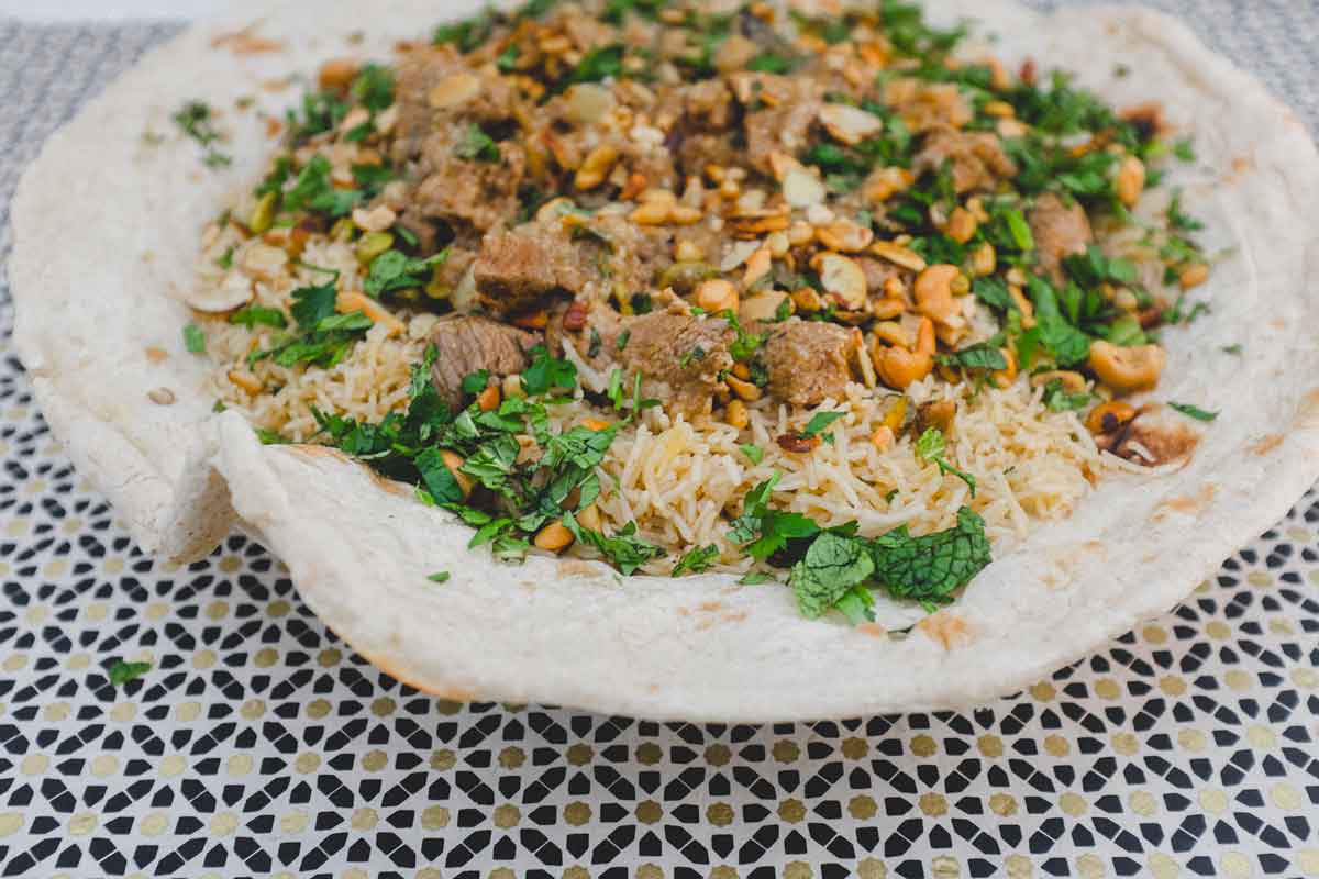 Jordanian lamb Mansaf stew sits on a giant flatbread. It's garnished with fresh herbs and toasted nuts.