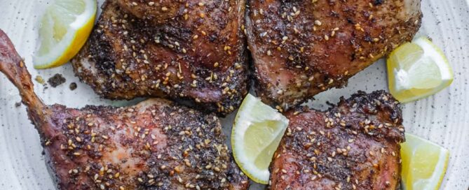 4 roasted duck legs with zaatar on a serving plate with small lemon wedges
