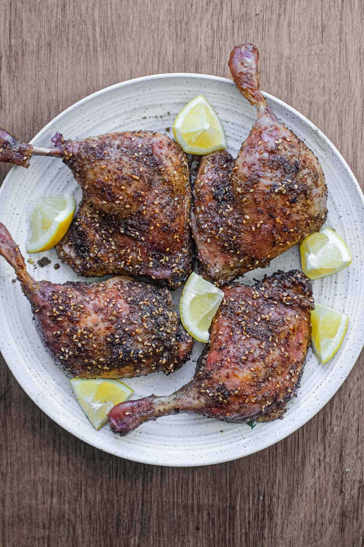 4 roasted duck legs with zaatar on a serving plate with small lemon wedges