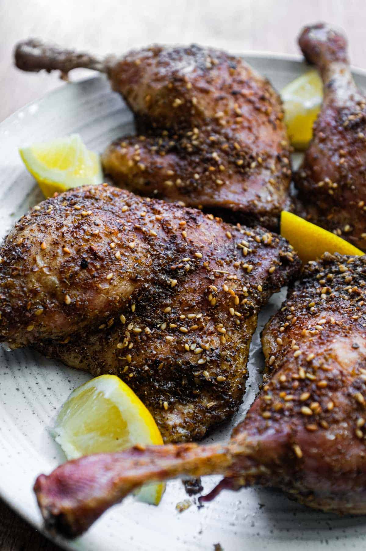 4 roasted duck legs with zaatar on a serving plate with small lemon wedges