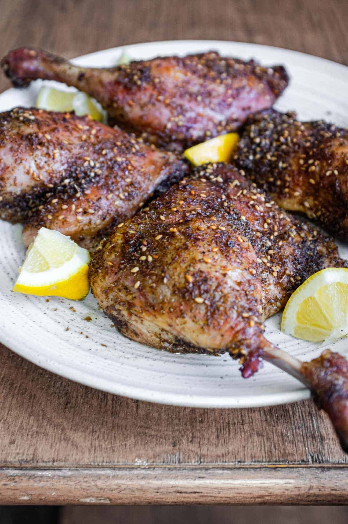 4 roasted duck legs with zaatar on a serving plate with small lemon wedges