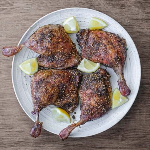 4 roasted duck legs with zaatar on a serving plate with small lemon wedges