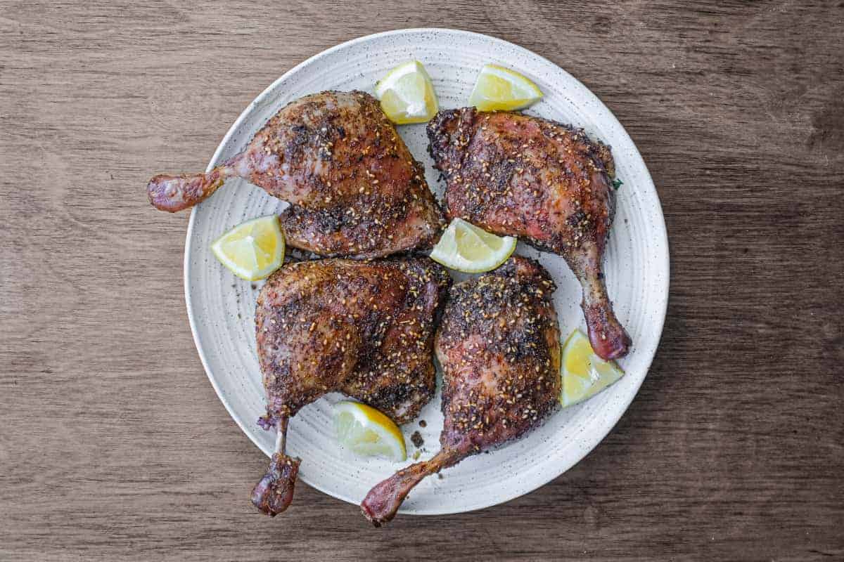 4 roasted duck legs with zaatar on a serving plate with small lemon wedges