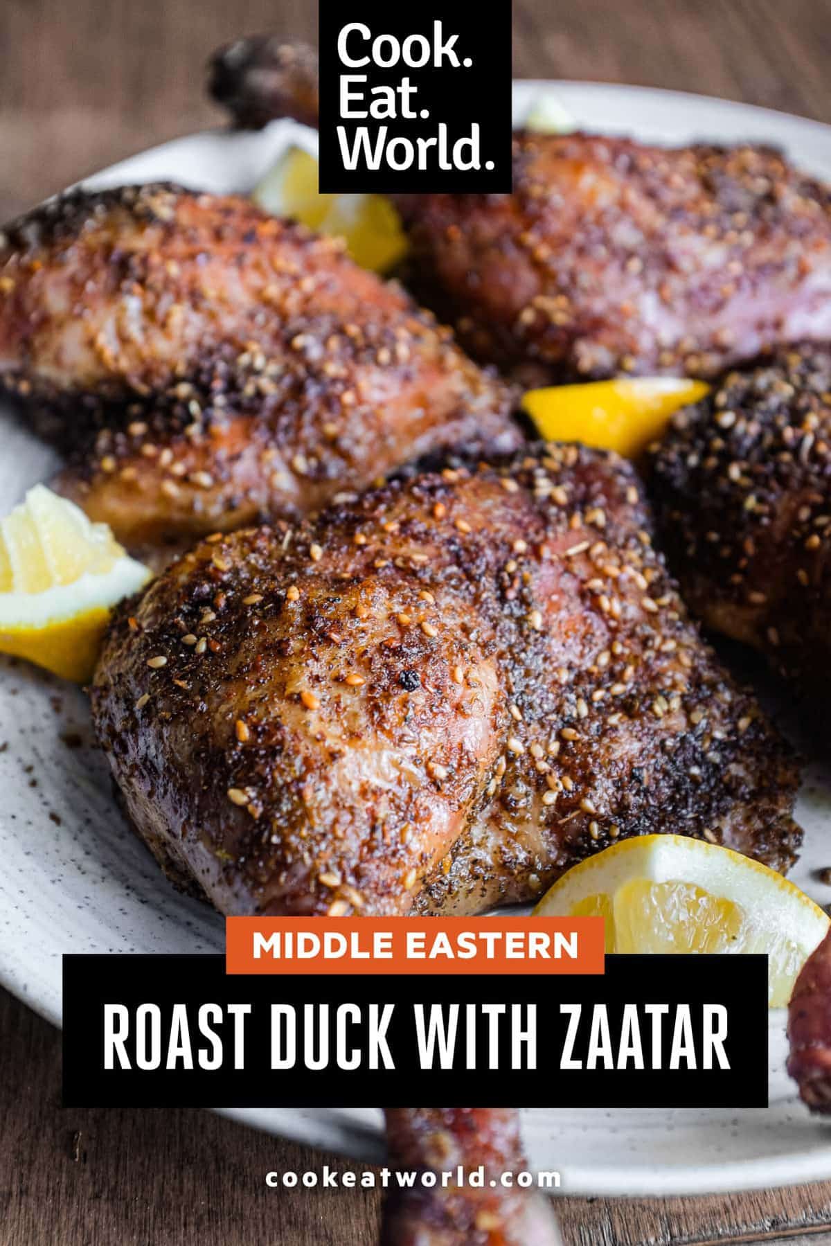 4 roasted duck legs with zaatar on a serving plate with small lemon wedges