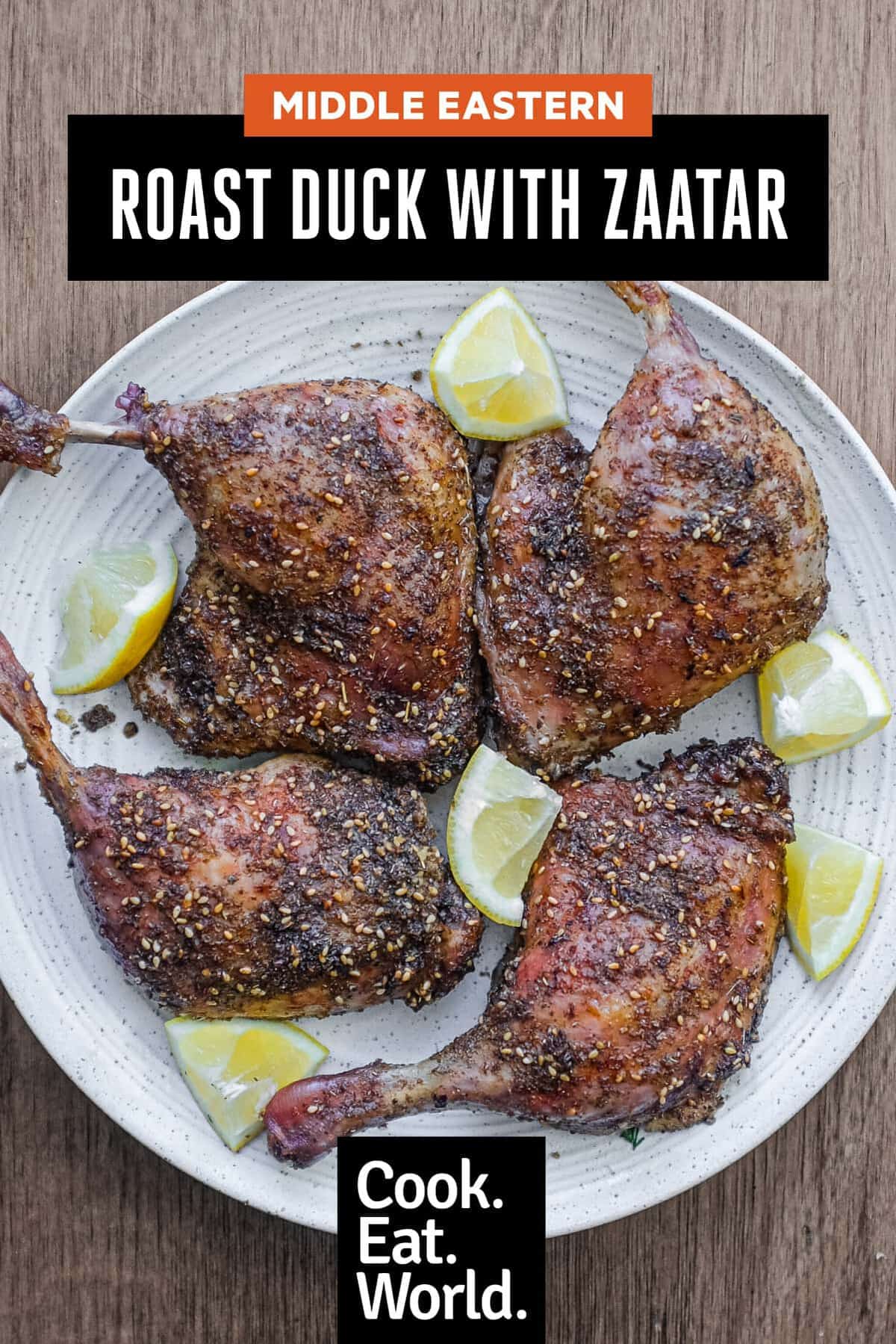 4 roasted duck legs with zaatar on a serving plate with small lemon wedges