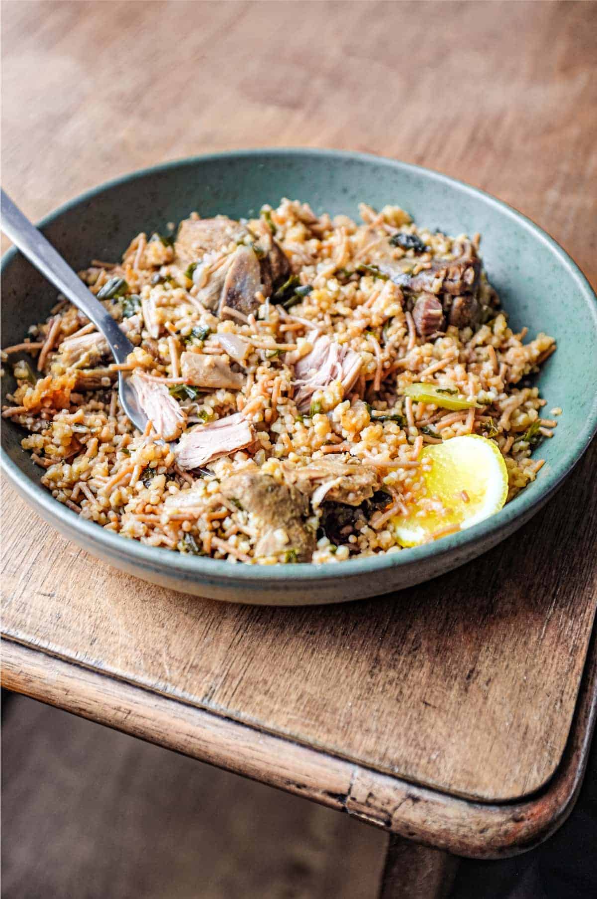 A bowl of Turkish bulgur pilav with a fork and a wedge of lemon.