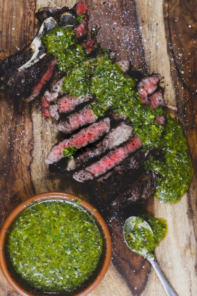 A wooden board with Argentinian Chimichurri Sauce and Steak