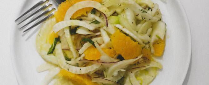 A plate of fennel & Orange Salad with a glass of white wine to the side.