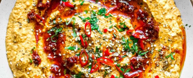 A bowl of Harissa Hummus garnished with chillies, chilli oil, zaatar and fresh cilantro.