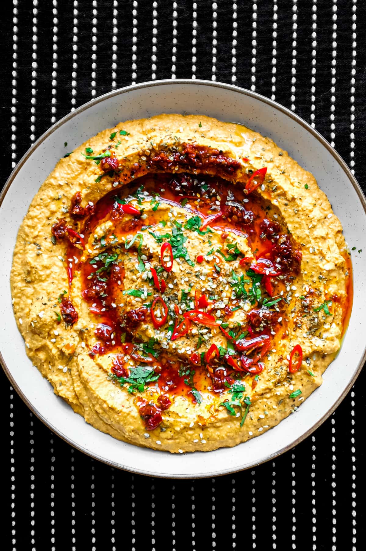 A bowl of Harissa Hummus garnished with chillies, chilli oil, zaatar and fresh cilantro.