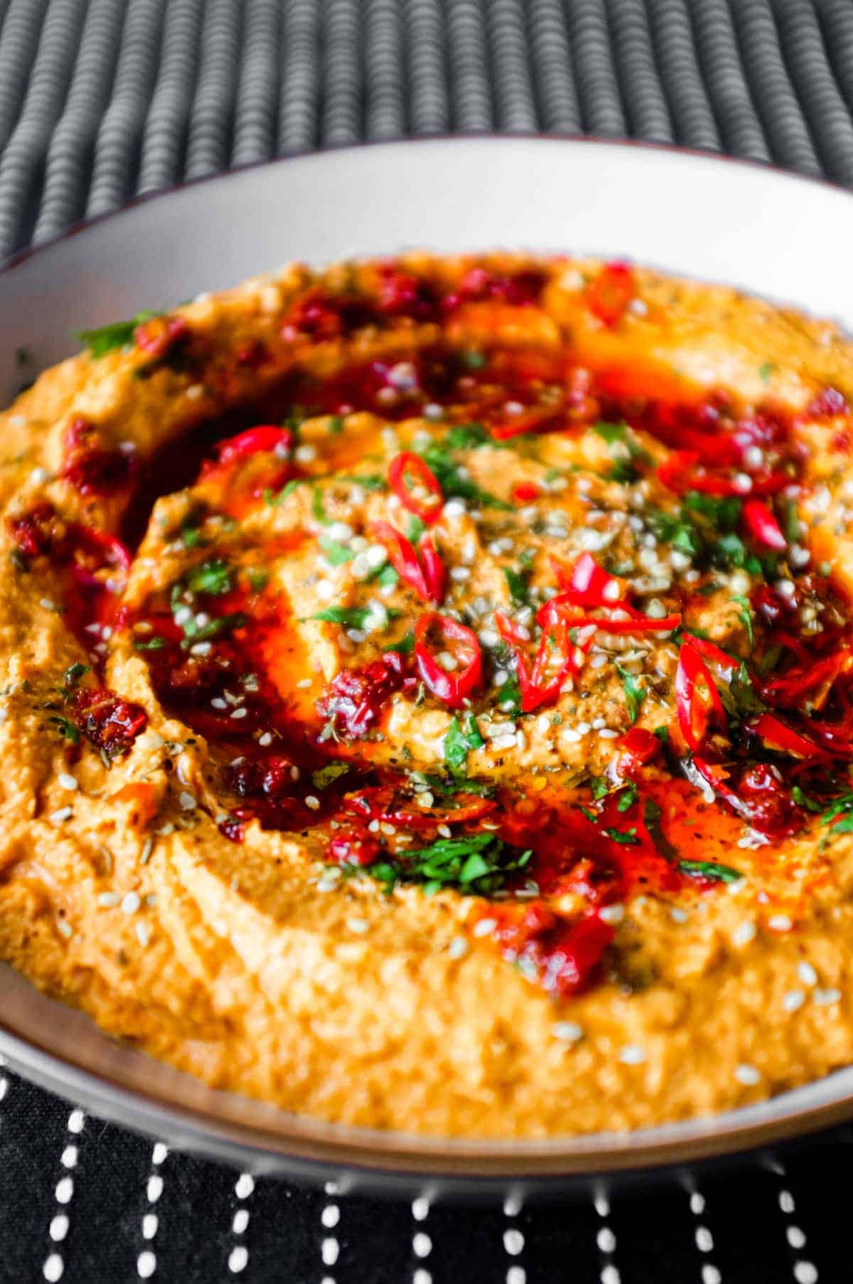 A bowl of Harissa Hummus garnished with chillies, chilli oil, zaatar and fresh cilantro.