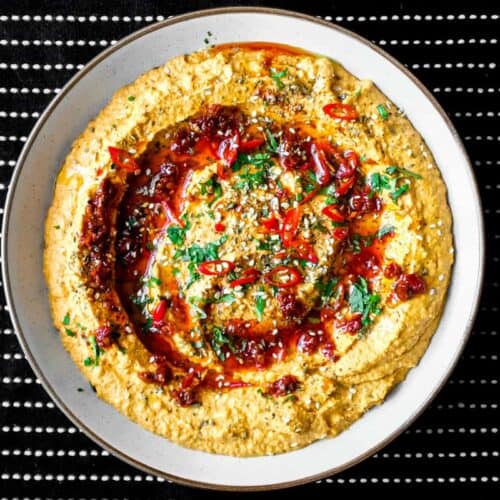A bowl of Harissa Hummus garnished with chillies, chilli oil, zaatar and fresh cilantro.