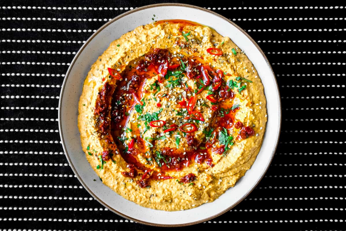 A bowl of Harissa Hummus garnished with chillies, chilli oil, zaatar and fresh cilantro.