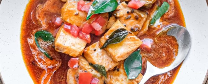 A bowl of Indian Salmon Curry decorated with fresh curry leaves, tomato and a drizzle of coconut cream