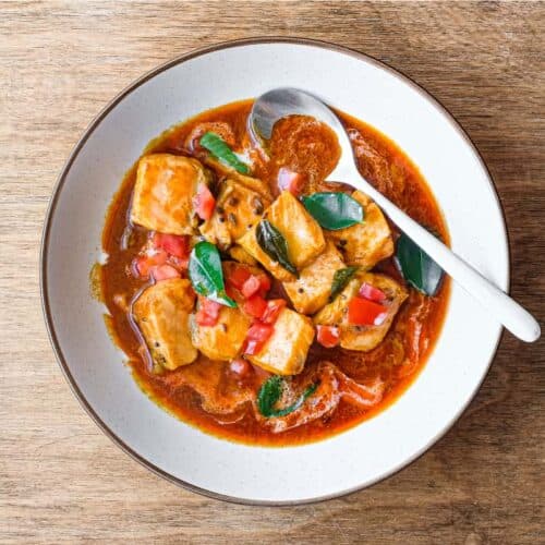 A bowl of Indian Salmon Curry decorated with fresh curry leaves, tomato and a drizzle of coconut cream