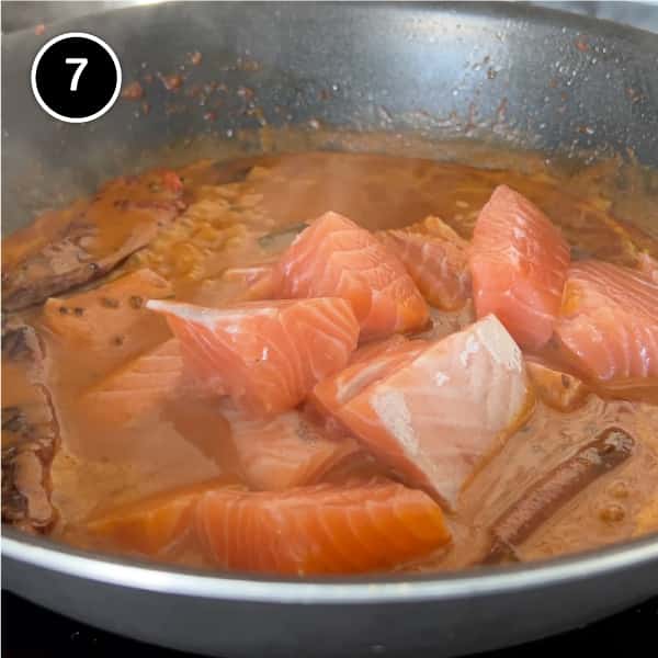 Fresh salmon being added to a coconut sauce