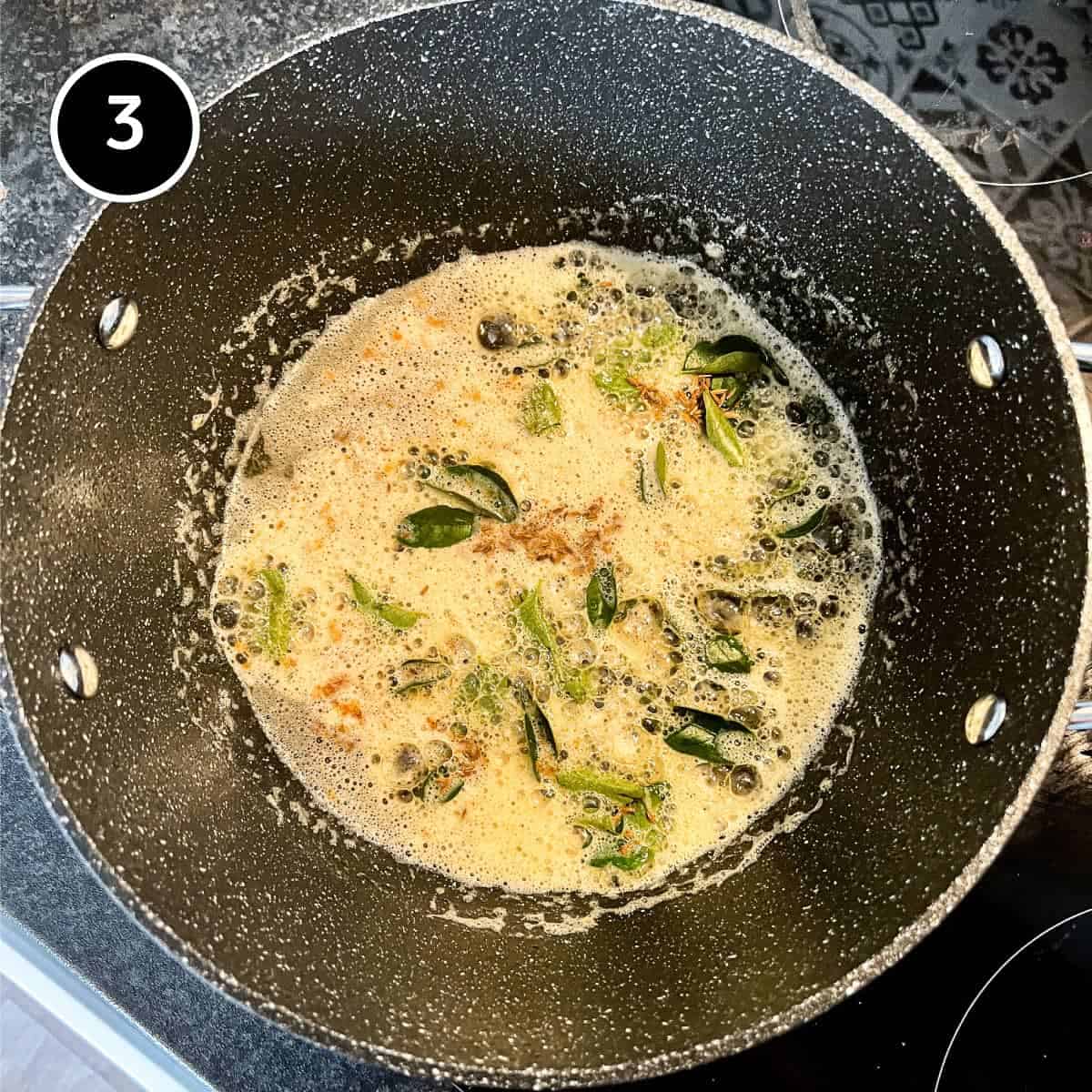 Curry leaves and cumin frying in ghee in a large pan