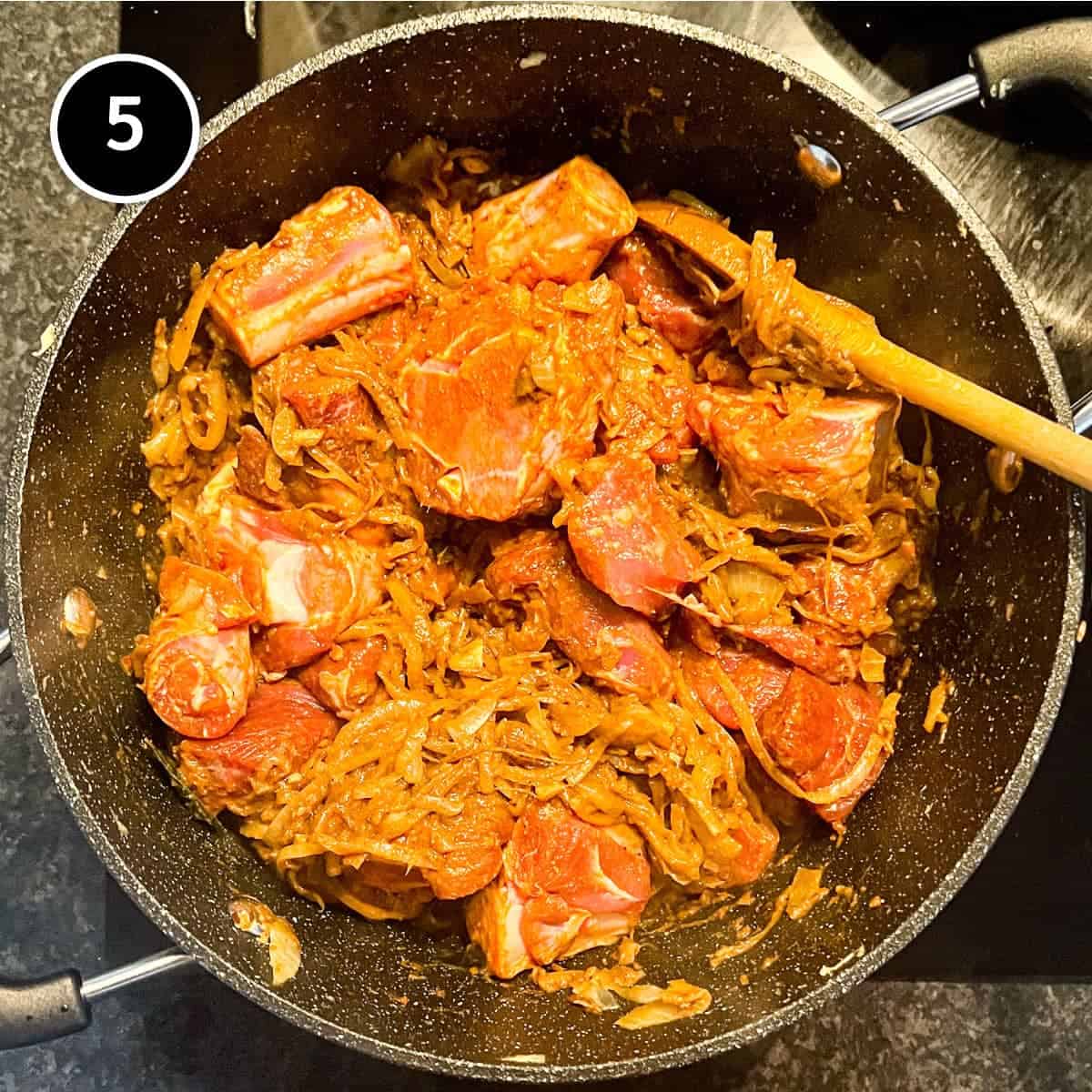 Madras spice paste and lamb is cooking in a large pan with onion