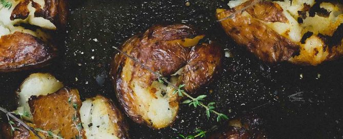 Punched potatoes on a baking sheet garnished with a little fresh thyme.