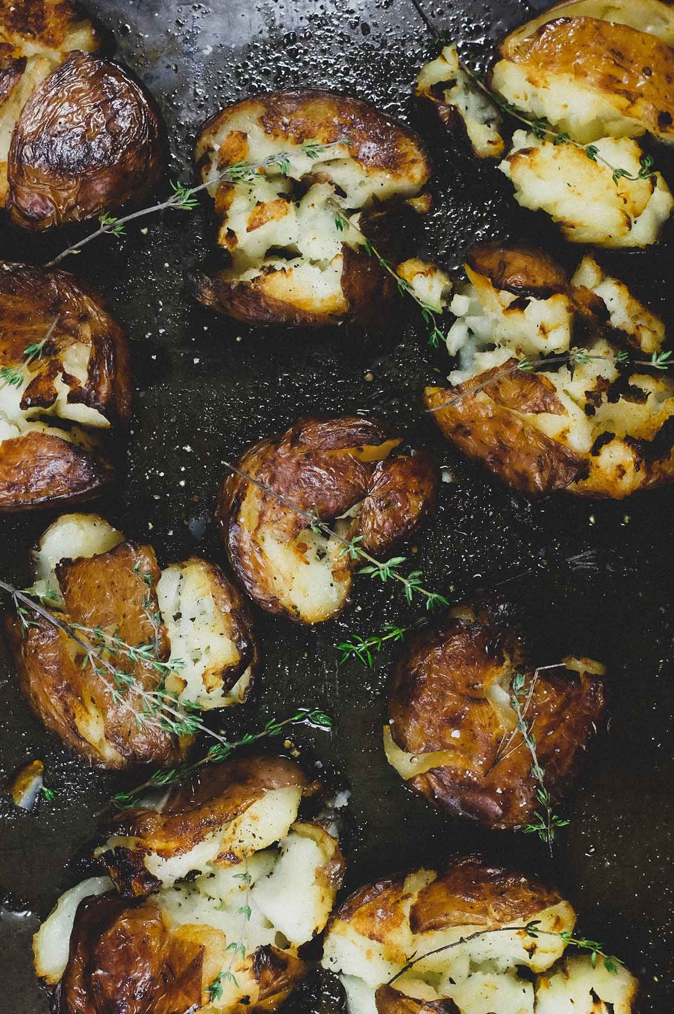 Punched potatoes on a baking sheet garnished with a little fresh thyme.