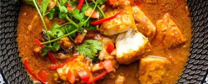 A bowl of Sri Lankan Fish Curry in a black bowl, garnished with cilantro and red chilli.
