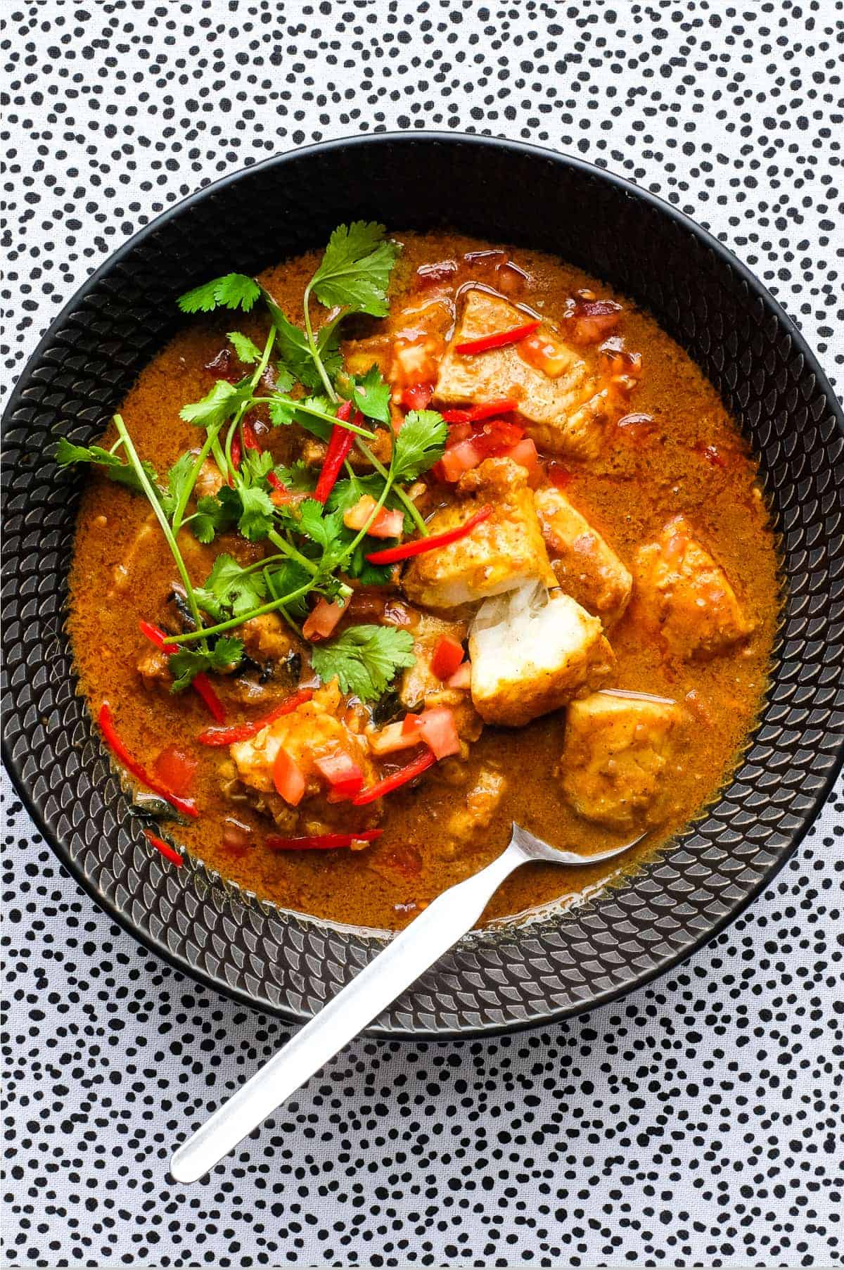 A bowl of Sri Lankan Fish Curry in a black bowl, garnished with cilantro and red chilli.