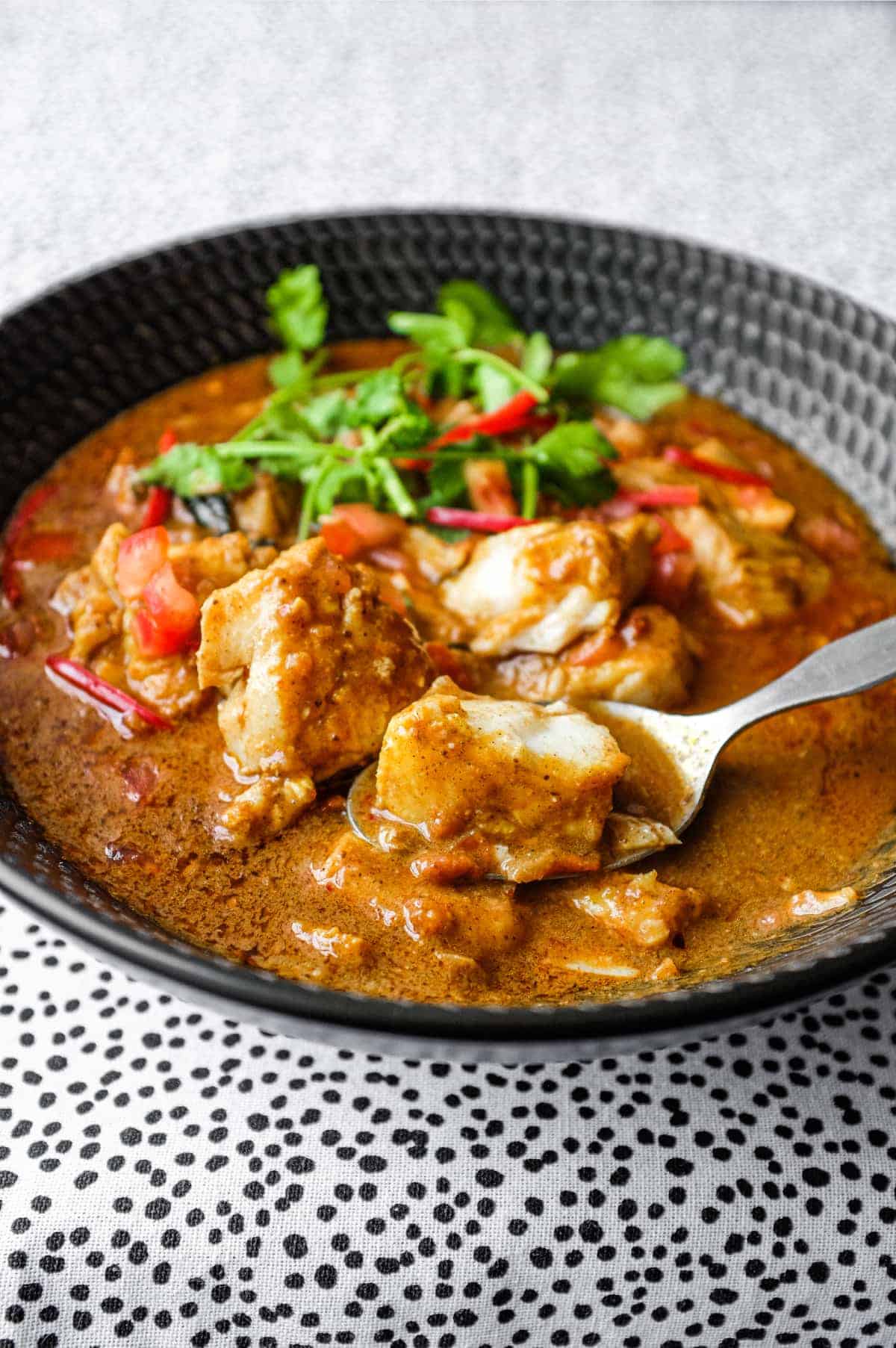 A bowl of Sri Lankan Fish Curry in a black bowl, garnished with cilantro and red chilli.