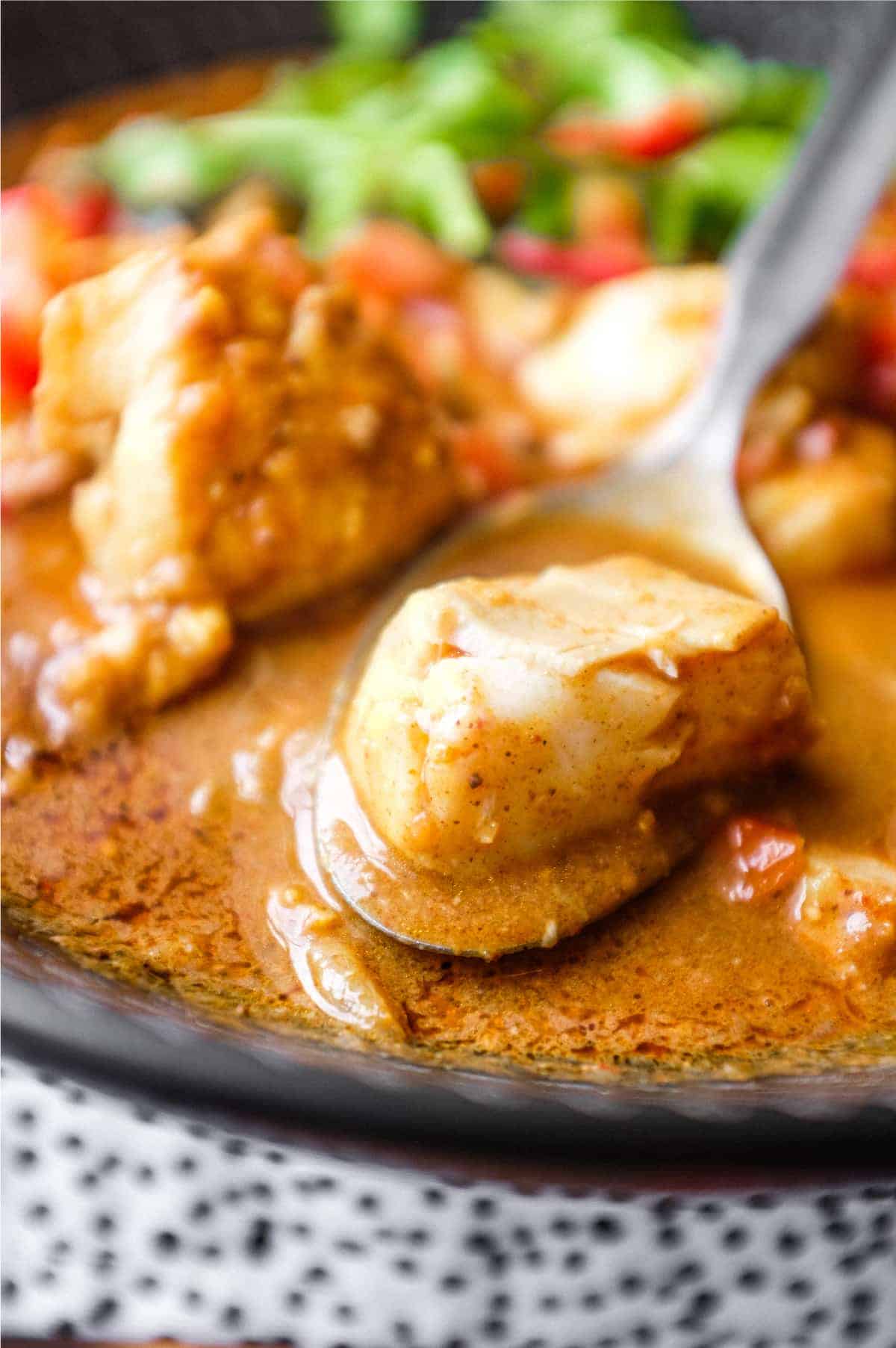 A bowl of Sri Lankan Fish Curry in a black bowl, garnished with cilantro and red chilli.