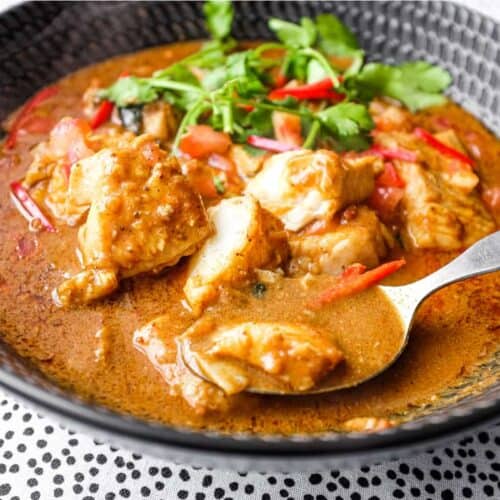 A bowl of Sri Lankan Fish Curry in a black bowl, garnished with cilantro and red chilli.
