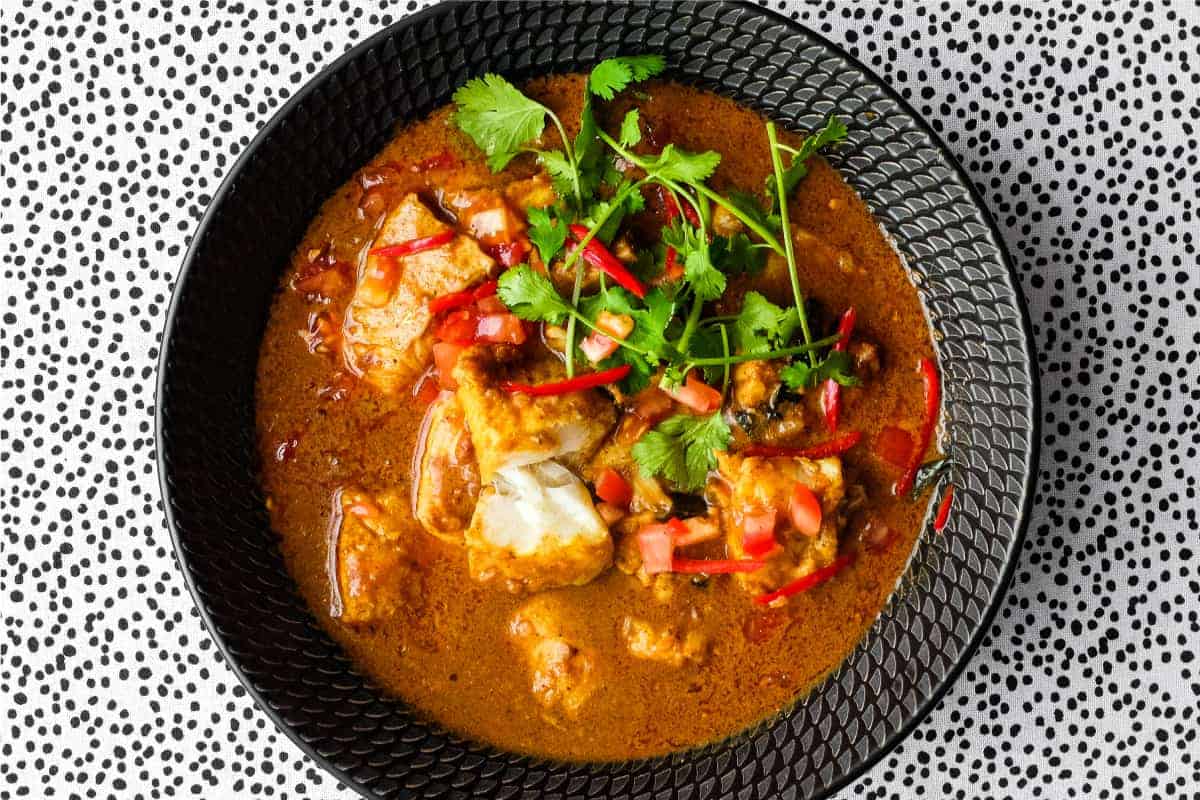 A bowl of Sri Lankan Fish Curry in a black bowl, garnished with cilantro and red chilli.