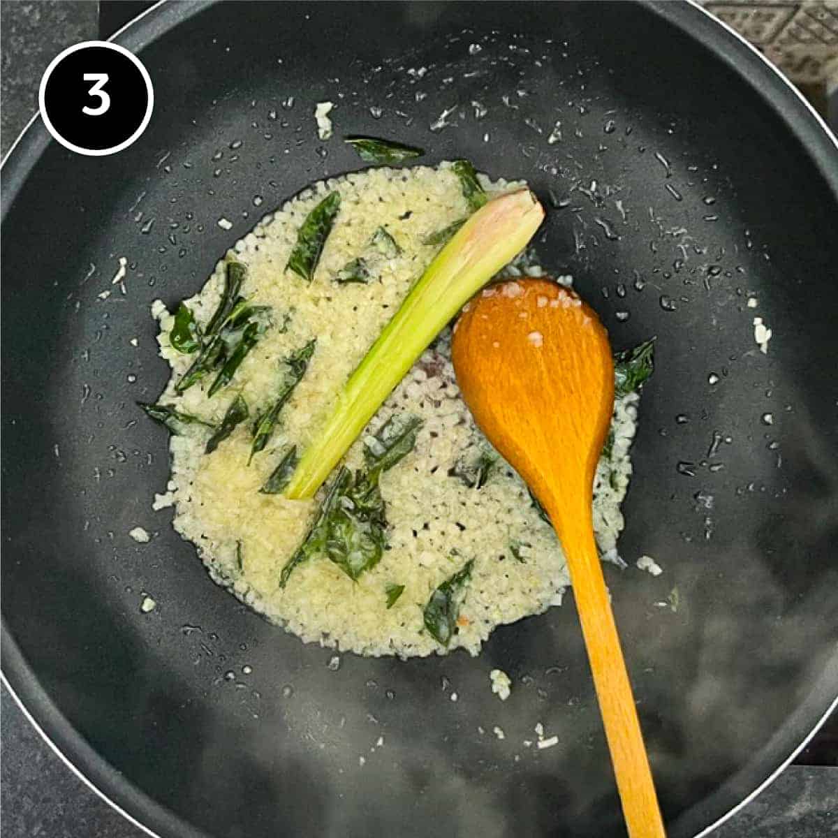 Onions, lemongrass and curry leaves frying in a pan with a wooden spoon