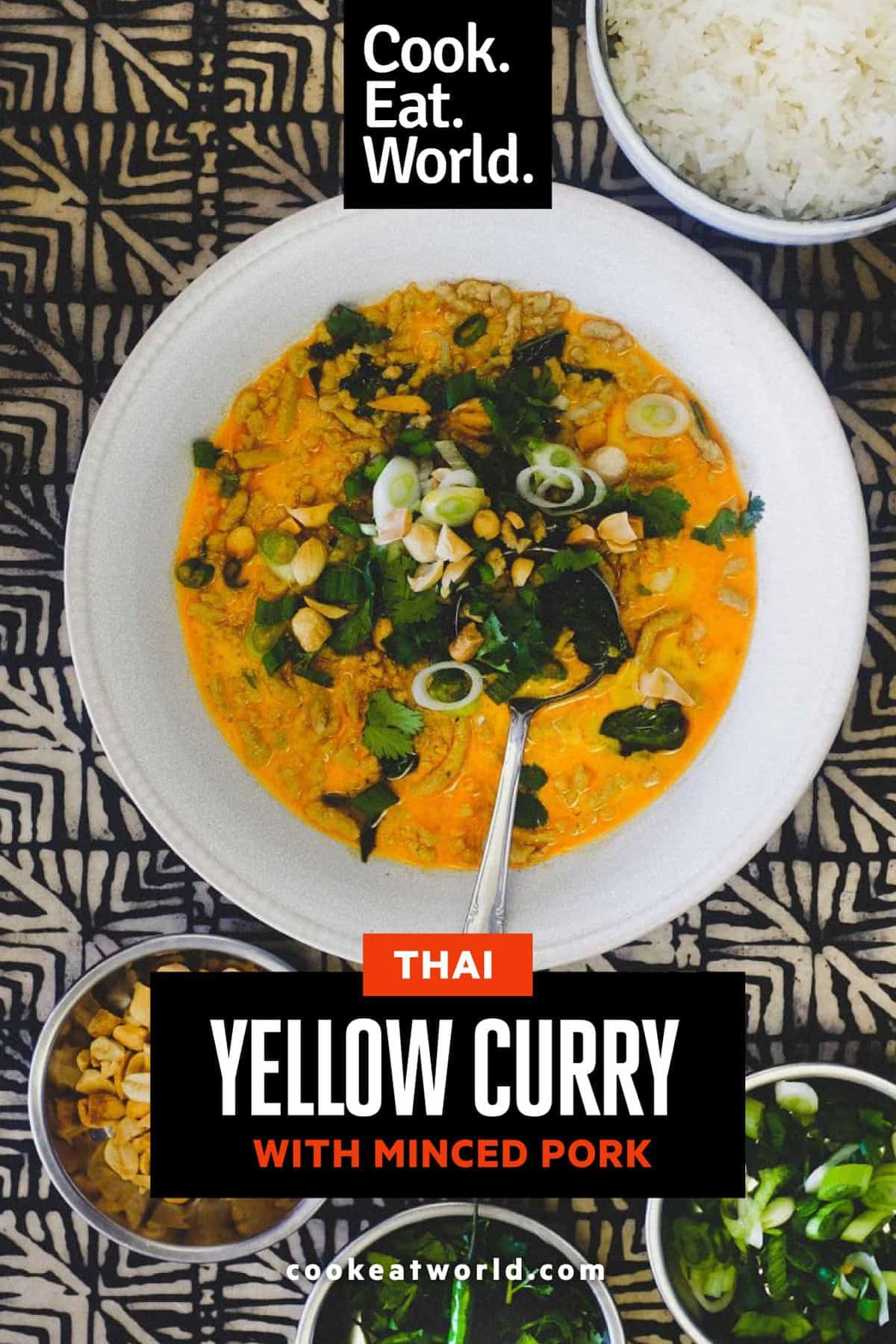 A bowl of Thai yellow curry with minced pork. Surrounding the bowl are smaller bowls of spring onions, cilantro, peanuts and jasmine rice.
