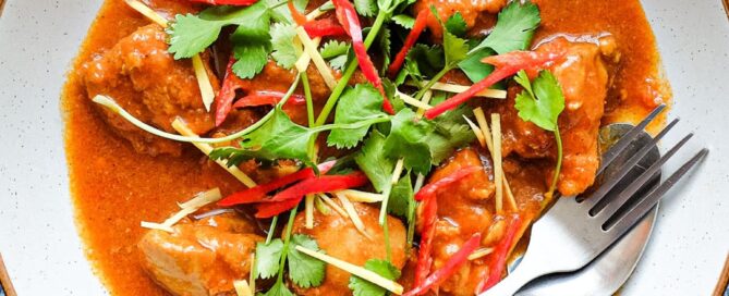 A bowl of Burmese chicken curry with fork and spoon