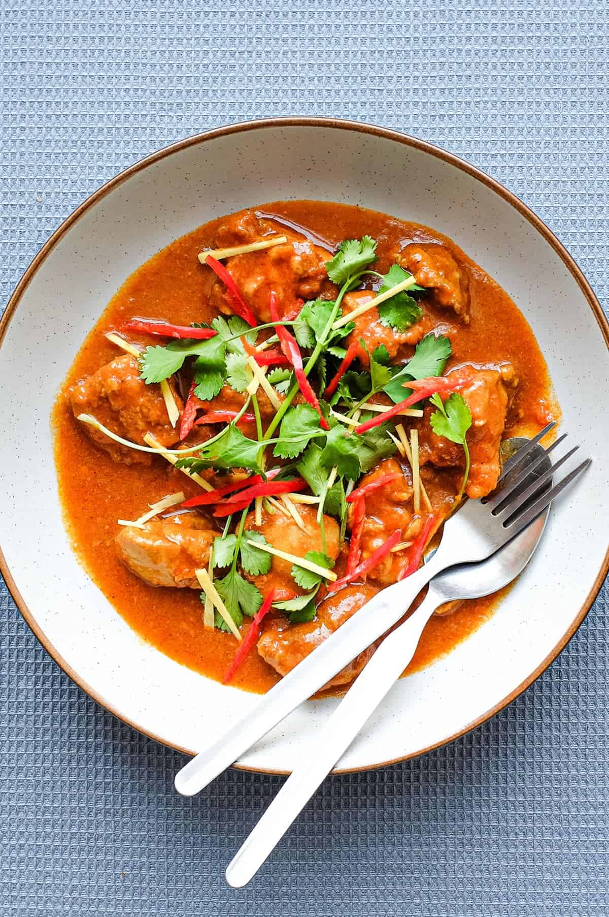 A bowl of Burmese chicken curry with fork and spoon